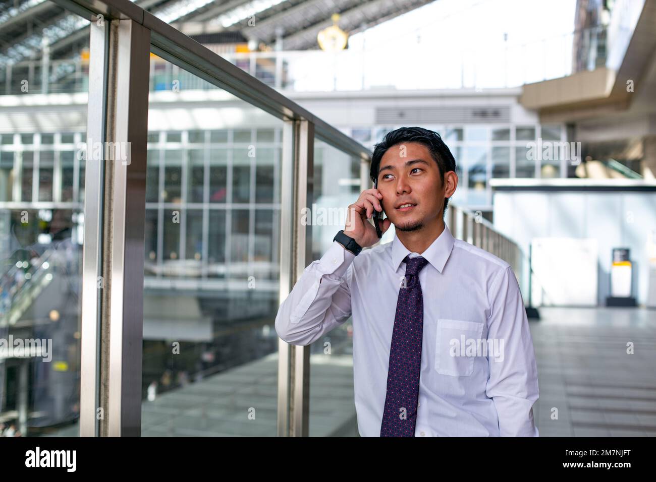 Un giovane uomo d'affari in città, in movimento, un uomo in una camicia bianca e cravatta sul suo telefono cellulare a piedi lungo un passaggio pedonale. Foto Stock