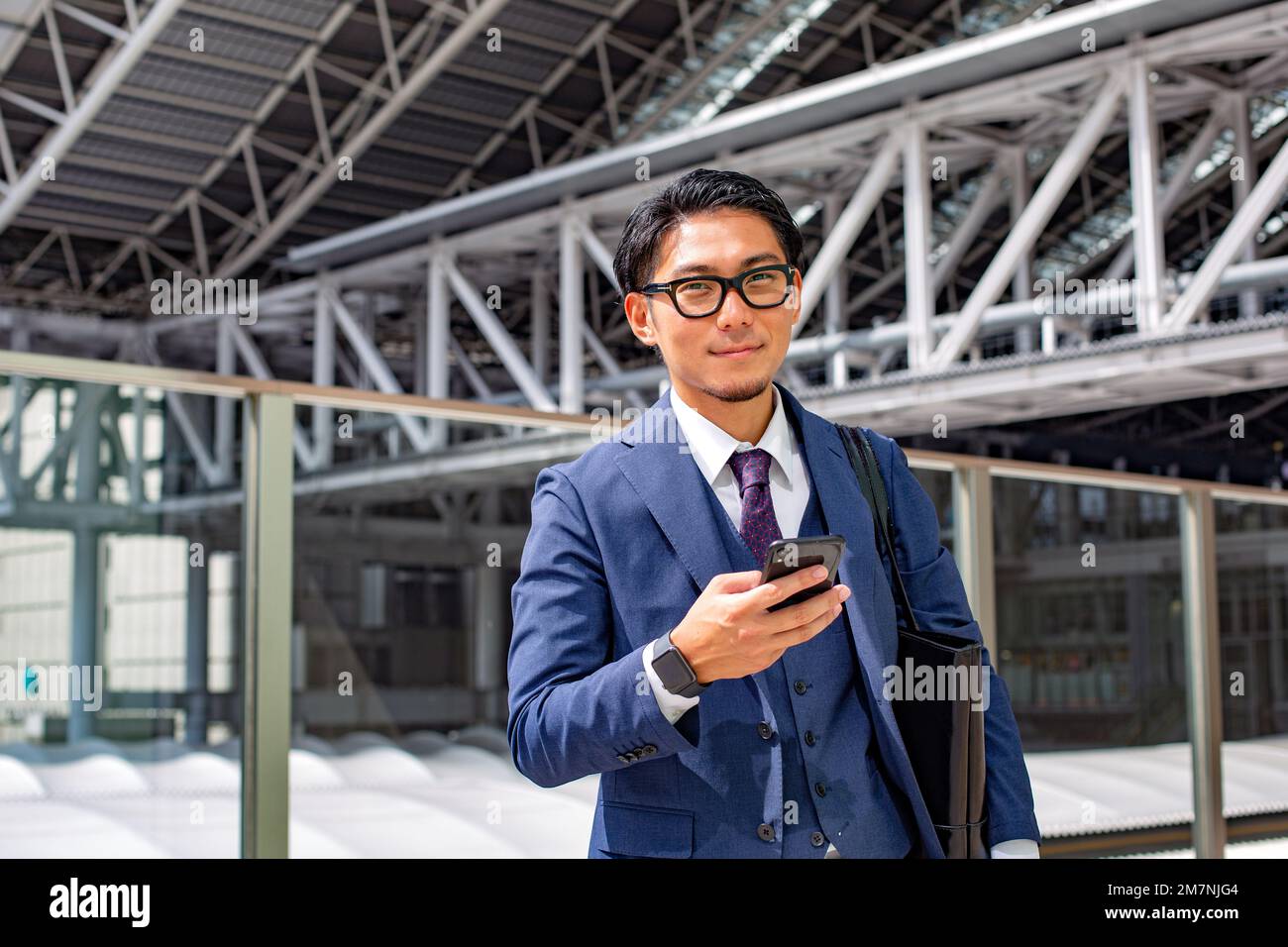 Un giovane uomo d'affari in città, in movimento, un uomo in tuta blu con una borsa per il computer portatile, che tiene un telefono cellulare. Foto Stock