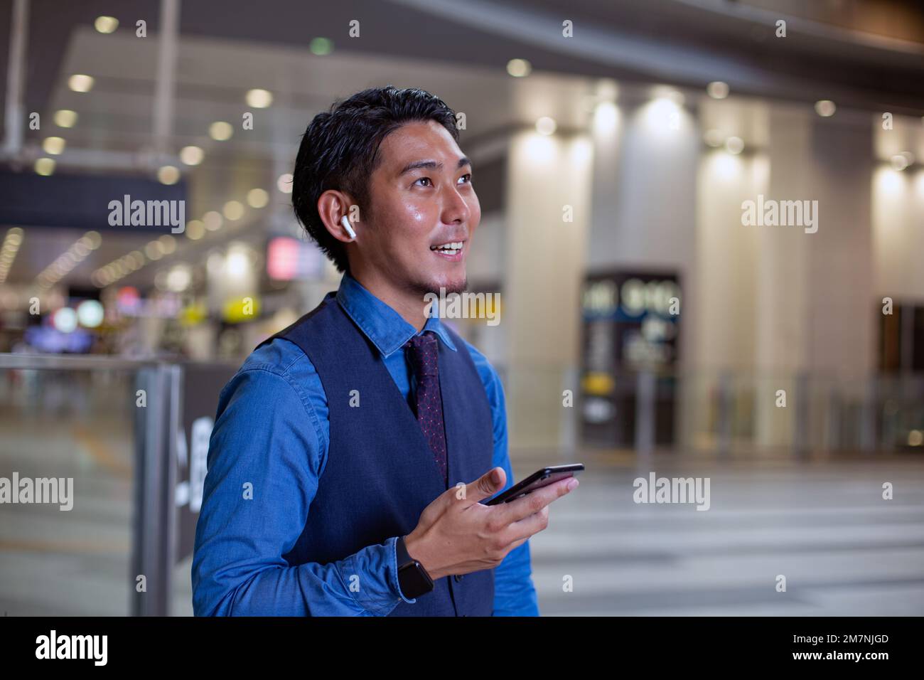 Un giovane uomo d'affari in città, in piedi guardando intorno, tenendo il suo telefono cellulare. Foto Stock