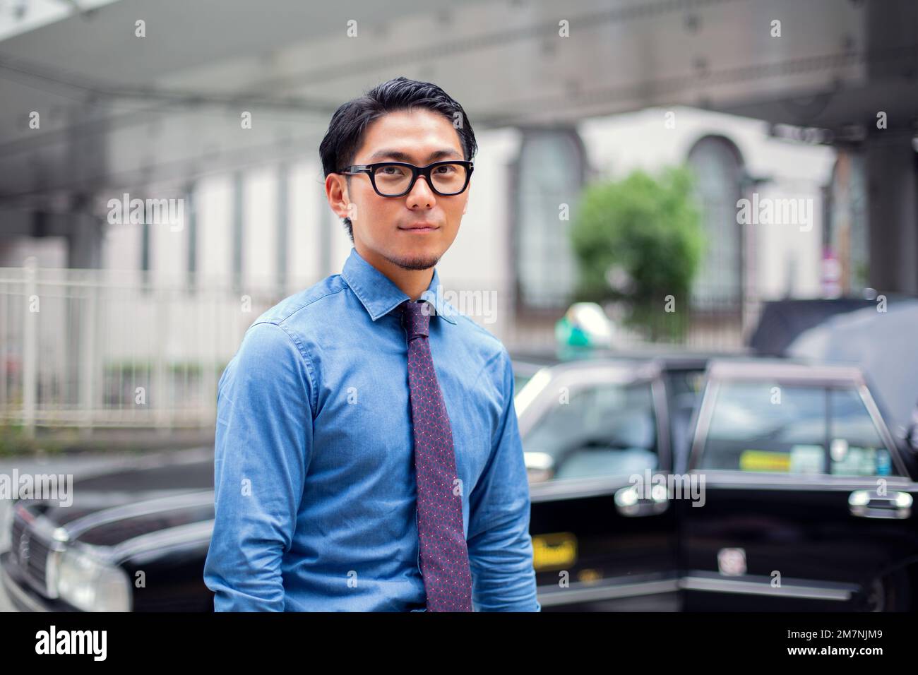 Un giovane uomo d'affari in città, in movimento, un uomo con occhiali, camicia e cravatta, un taxi dietro di lui. Foto Stock