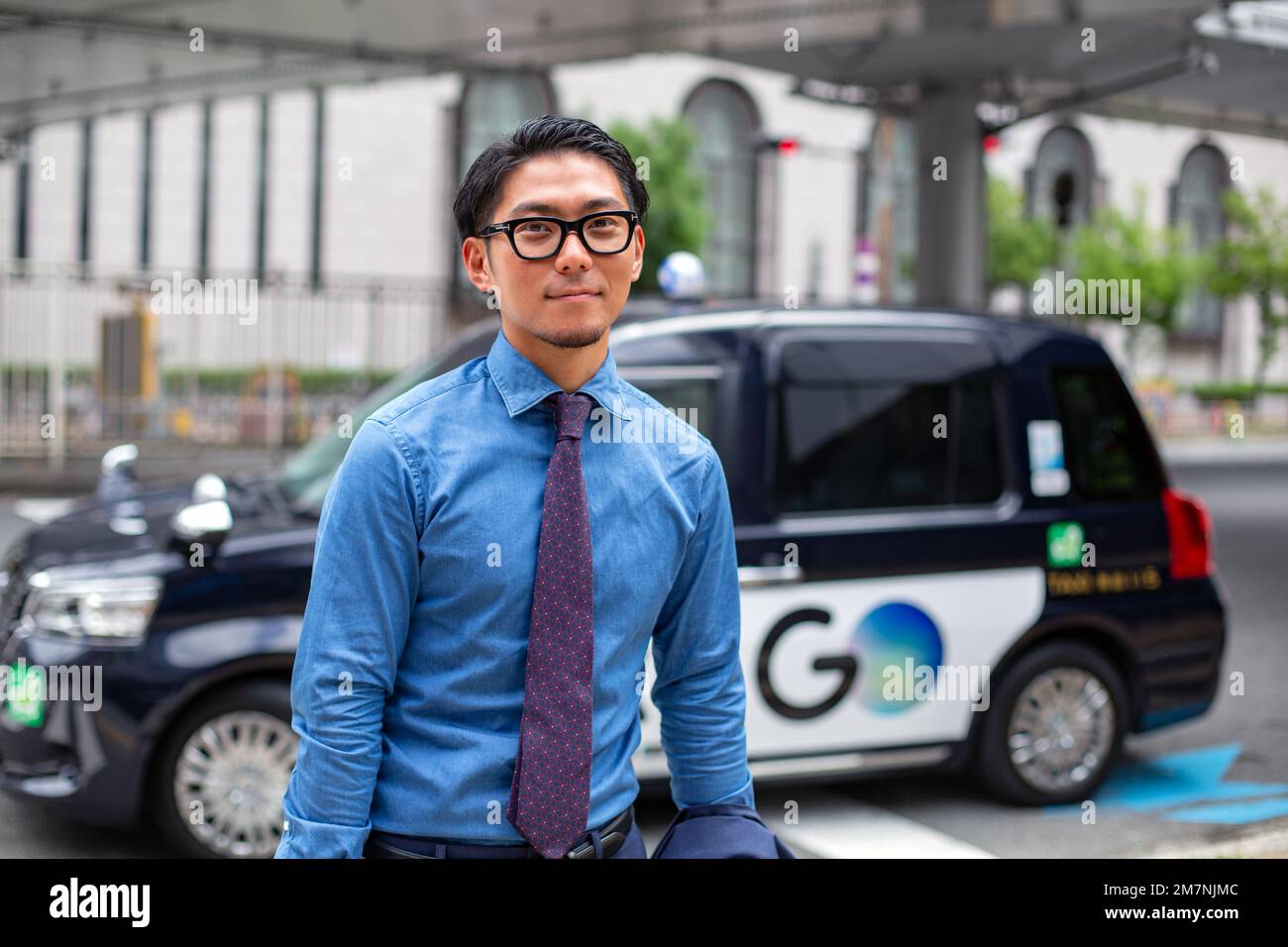Un giovane uomo d'affari in città, in movimento, un uomo con occhiali, camicia e cravatta, un taxi dietro di lui. Foto Stock