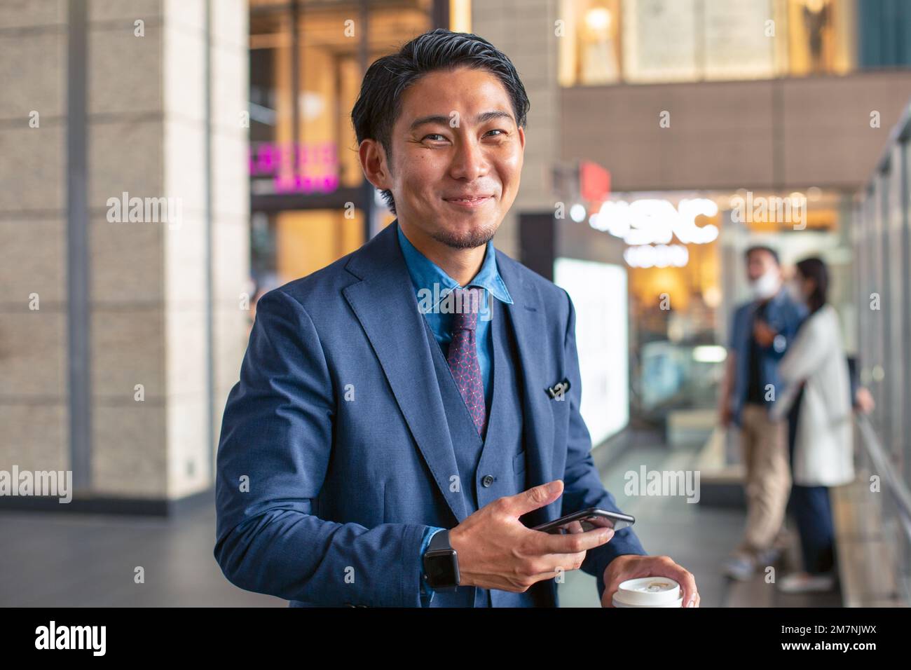 Un giovane uomo d'affari in tuta blu in movimento in una zona del centro città, tenendo il suo telefono cellulare. Foto Stock