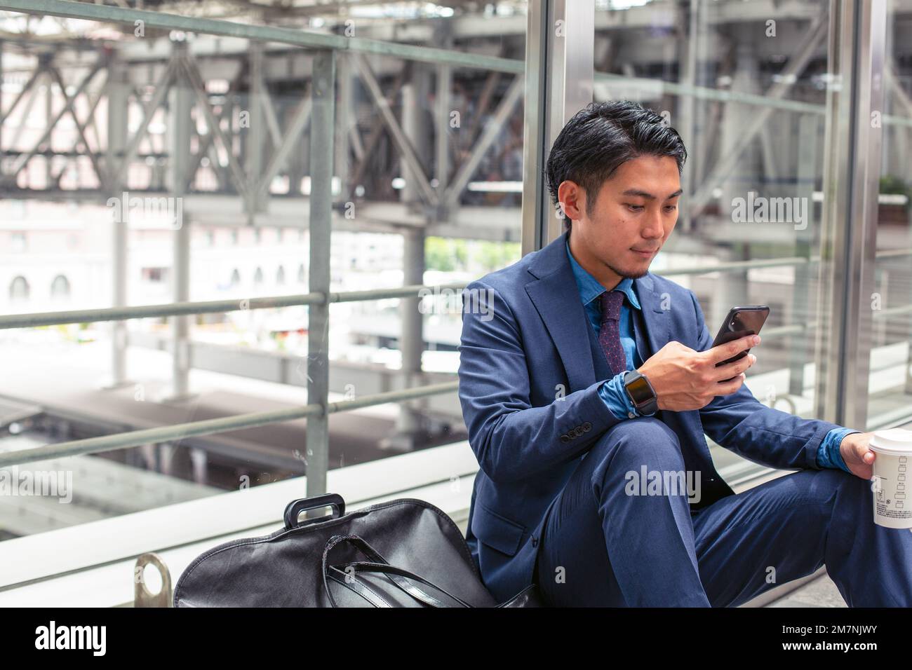 Un giovane uomo d'affari in una tuta blu in una città, guardando lo schermo del suo telefono cellulare, testando o leggendo un messaggio. Foto Stock