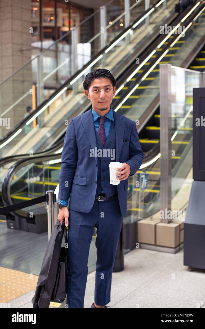Un giovane uomo d'affari in tuta blu in movimento in una zona del centro città, con una valigetta e una tazza di caffè. Foto Stock