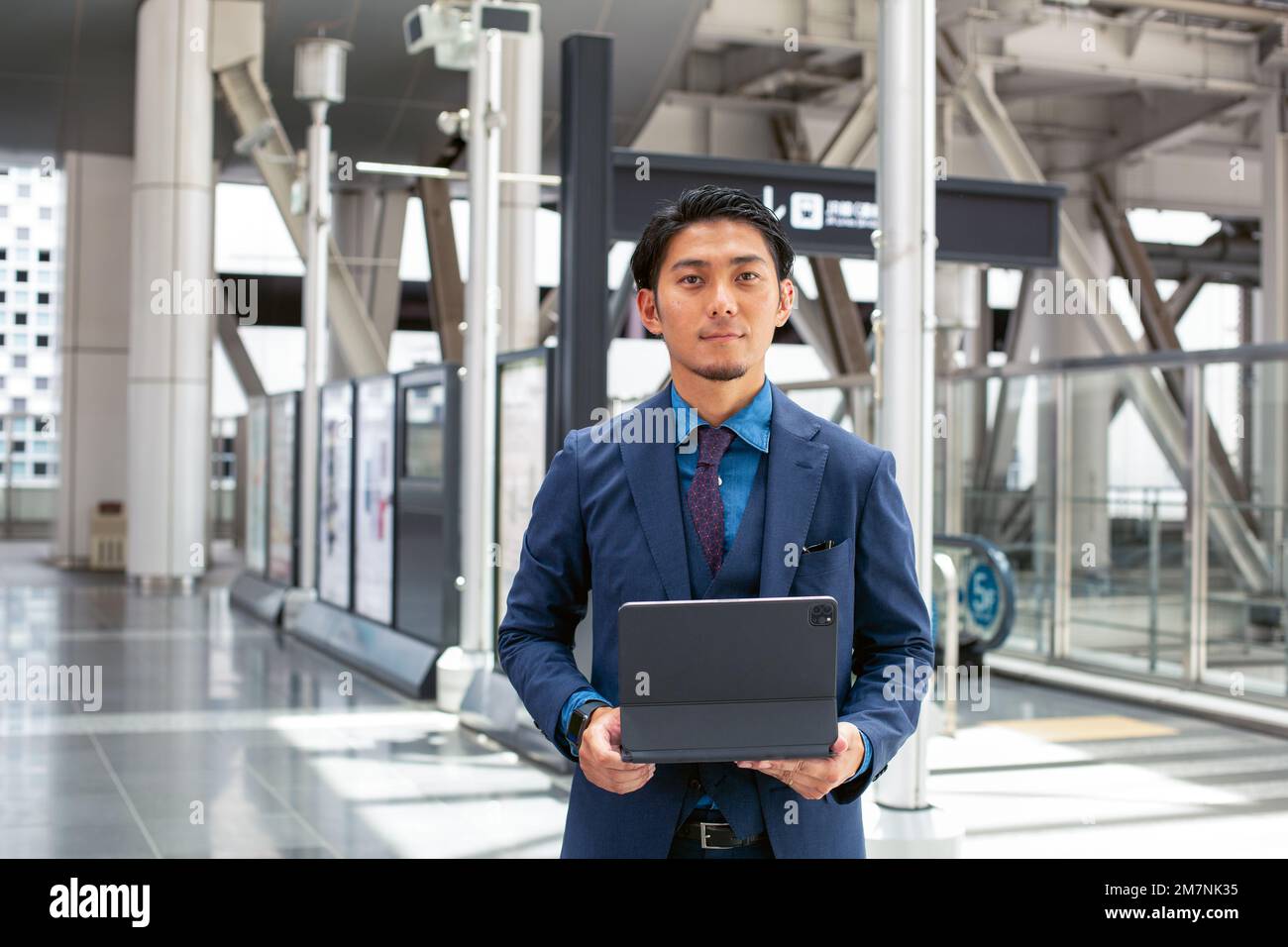 Un giovane uomo d'affari in tuta blu in movimento in una zona del centro città, in piedi e utilizzando il suo tablet digitale. Foto Stock