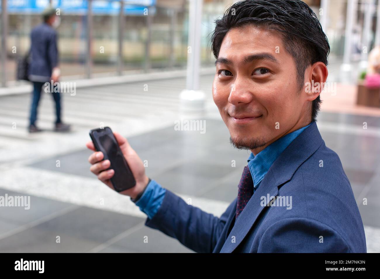 Un giovane uomo d'affari in tuta blu in movimento in una zona del centro città, tenendo il suo telefono cellulare. Foto Stock