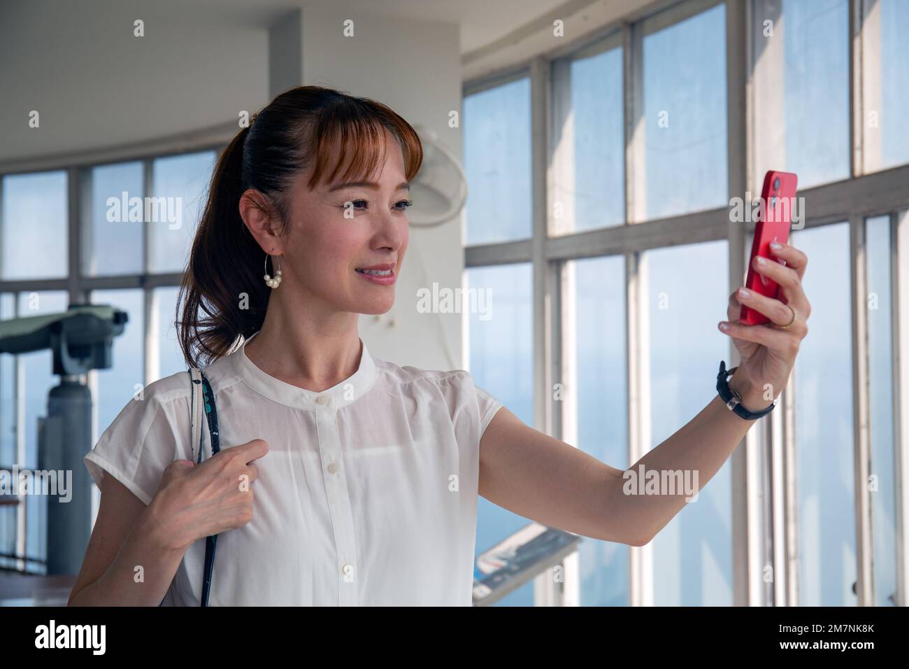Una donna giapponese matura che utilizza il suo telefono cellulare per scattare foto da una piattaforma di osservazione della città e del paesaggio sottostante. Foto Stock