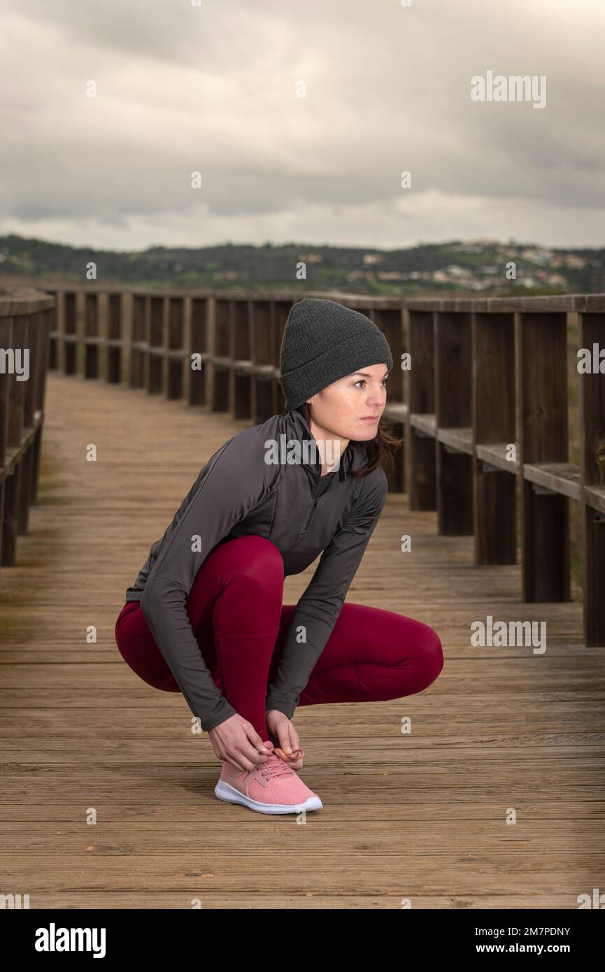 Jogger femminile che lega la sua scarpa, preperazione per una corsa su una passerella di legno Foto Stock