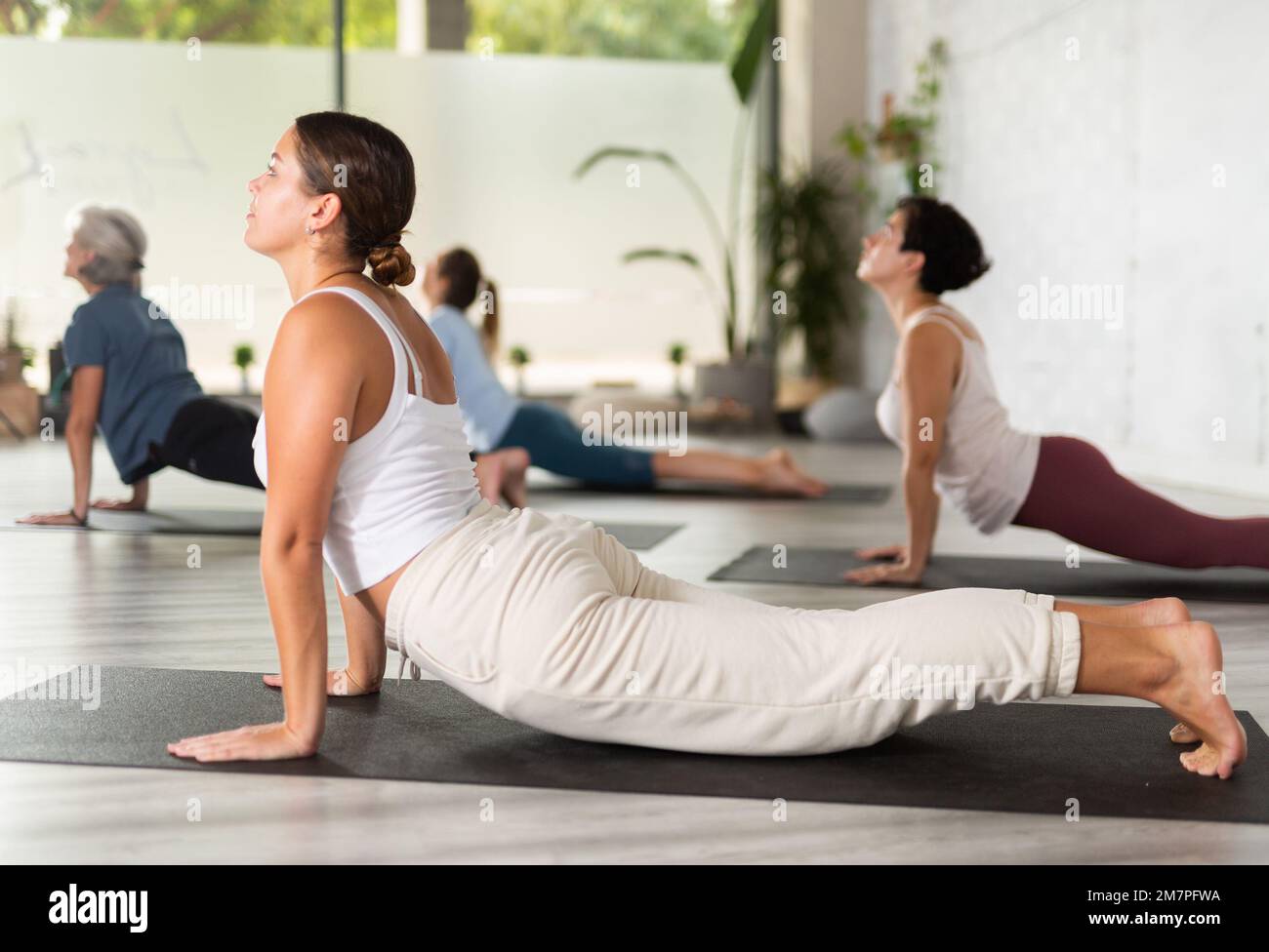 Gruppo di donne sportive che esercitano la classe di yoga facendo Bhujangasana (Cobra stretch posa) nel moderno centro fitness. Attenzione alle giovani donne Foto Stock