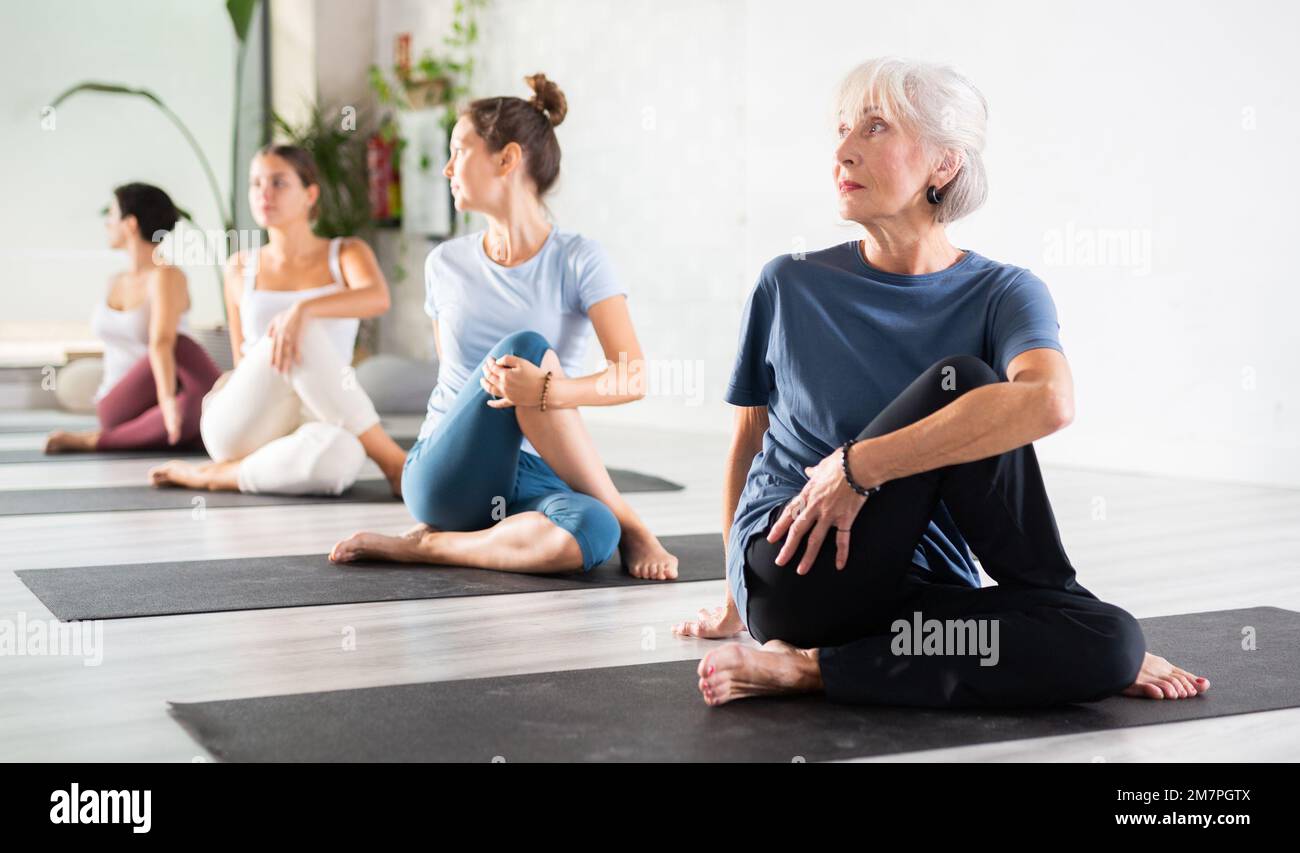 Donna anziana che mantiene la salute mentale e fisica frequentando classe di yoga di gruppo in studio, praticando pose stretching Foto Stock