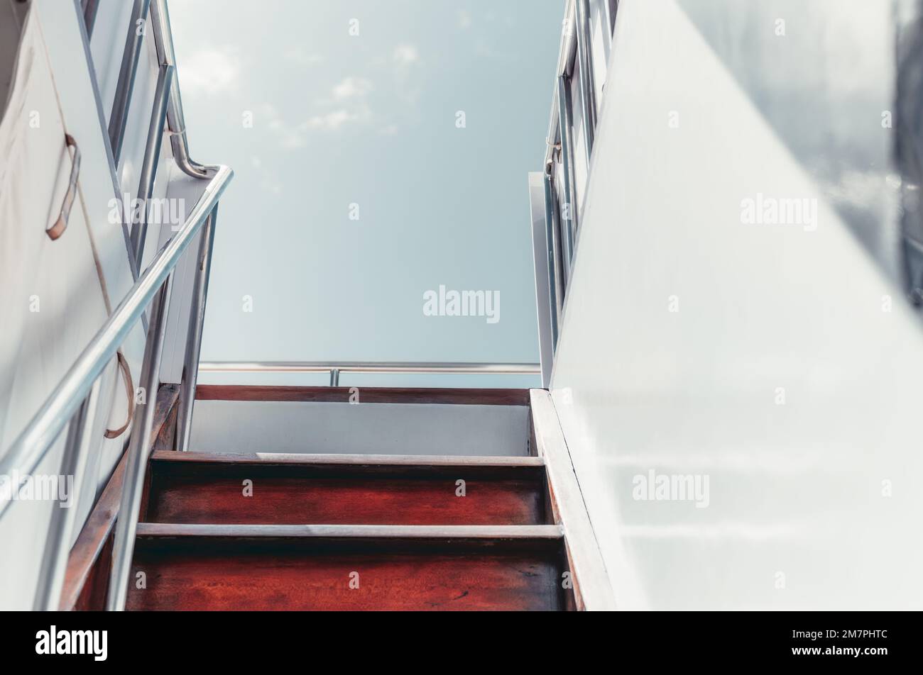 Uno scatto catturato dal ponte inferiore quando si sale una scala in legno e scintillanti ringhiere metalliche che conducono al ponte superiore di uno yacht a vela bianco; su Foto Stock