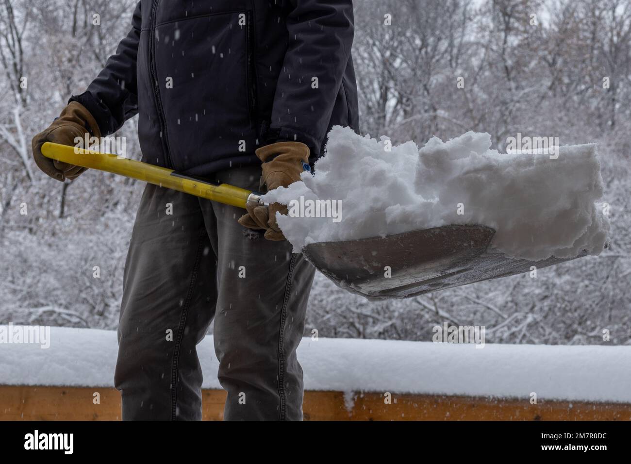 Primo piano vista parziale di un uomo adulto con una pala piena di neve su un ponte di legno in una giornata invernale sovrastata Foto Stock