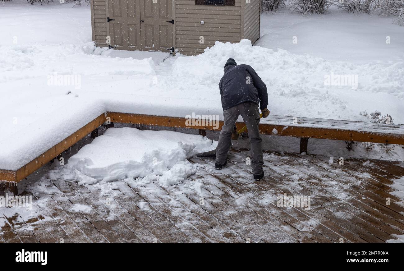Vista ad angolo alto di un uomo adulto che spalma la neve profonda su un ponte di legno in una giornata invernale Foto Stock