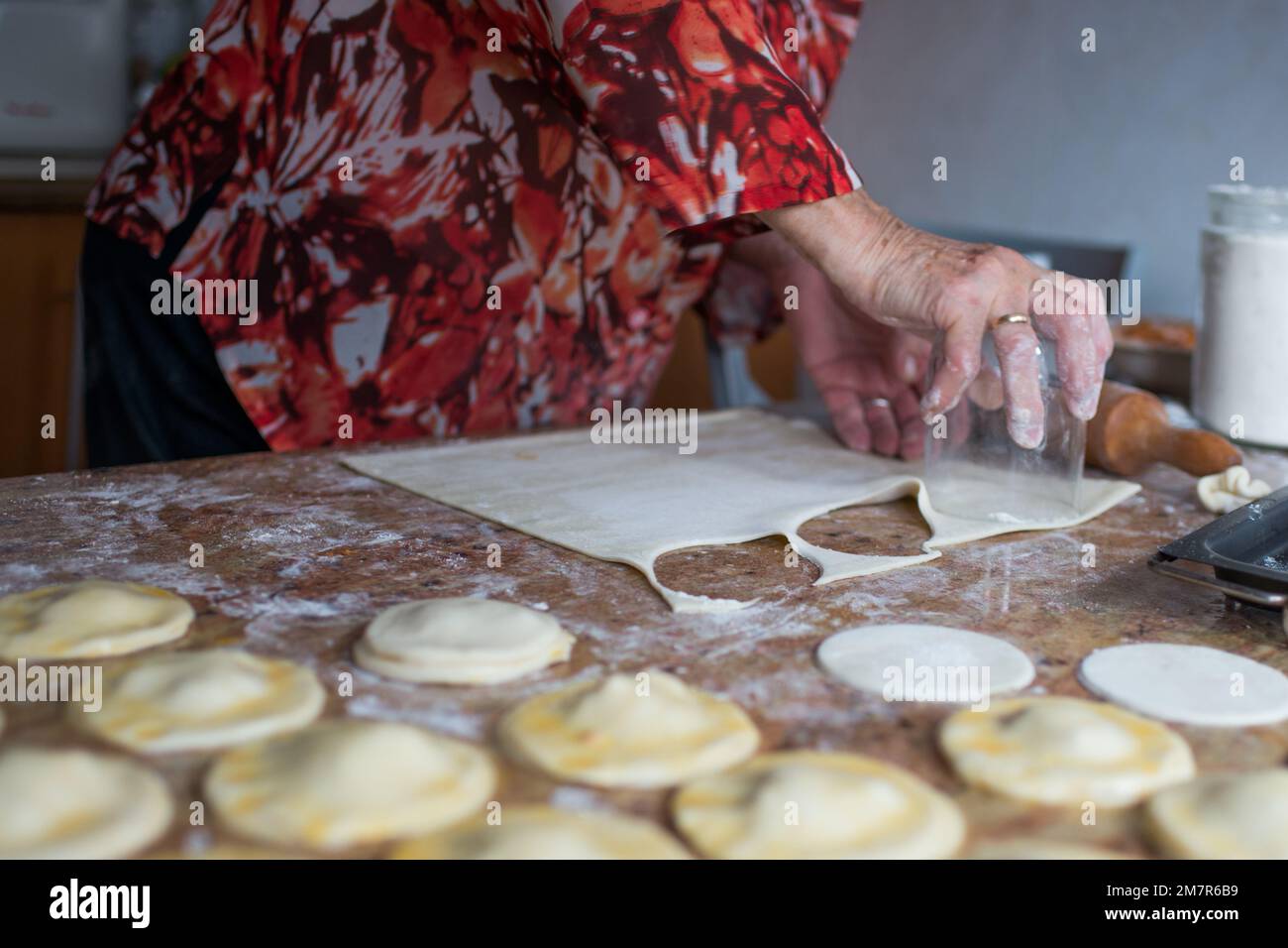 Donna anziana irriconoscibile che taglia pasta sfoglia con un bicchiere per preparare gnocchi. Spagna Foto Stock