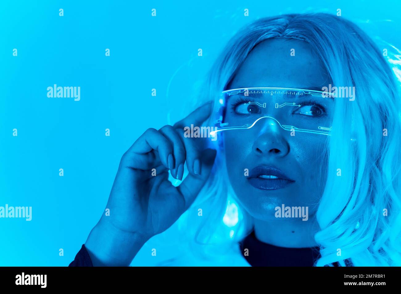 Concetto futuristico, una giovane donna in occhiali di realtà virtuale su sfondo blu Foto Stock