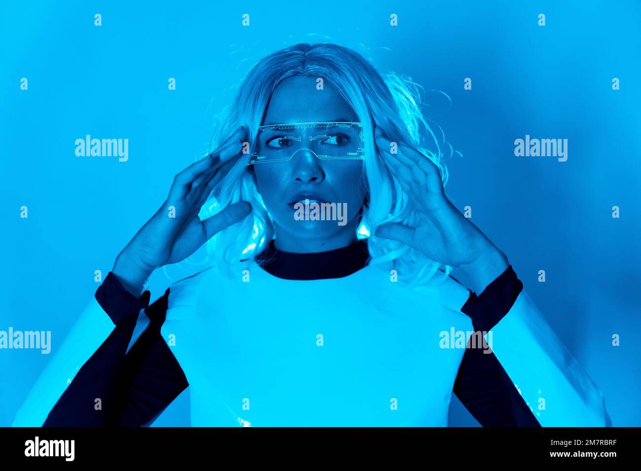 Concetto futuristico, una giovane ragazza in occhiali dal futuro su sfondo blu, cyberpunk, realtà virtuale Foto Stock
