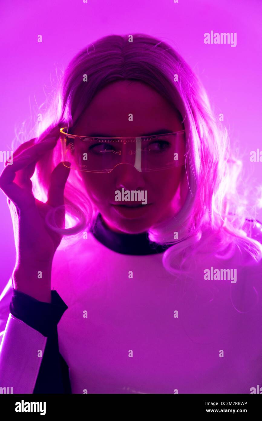 Una donna in costume futuristico e occhiali con luci rosa, concetto virtuale o metaverse, foto verticale Foto Stock
