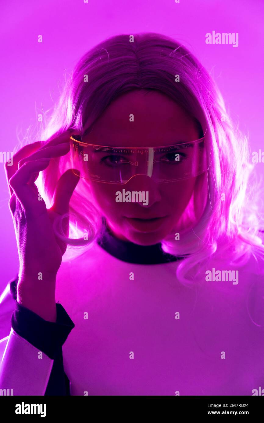 Una donna in un abito futuristico e occhiali con luci rosa, virtuale o concetto metaverse Foto Stock