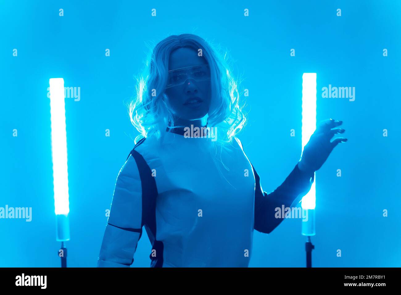 Giovane donna in costume futuristico e occhiali con luci a LED blu, virtuale o metaverse concetto Foto Stock