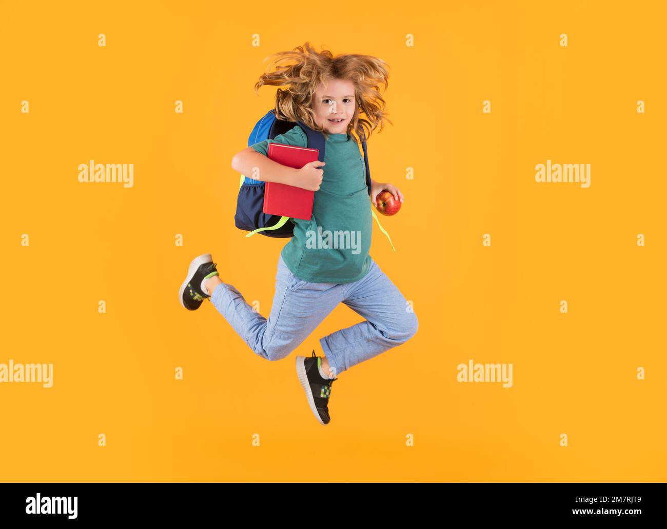 Corpo a tutta lunghezza di bambino piccolo scuola che salta avendo divertente sfondo di colore giallo isolato. Crazy scuola ragazzo salto. Foto Stock