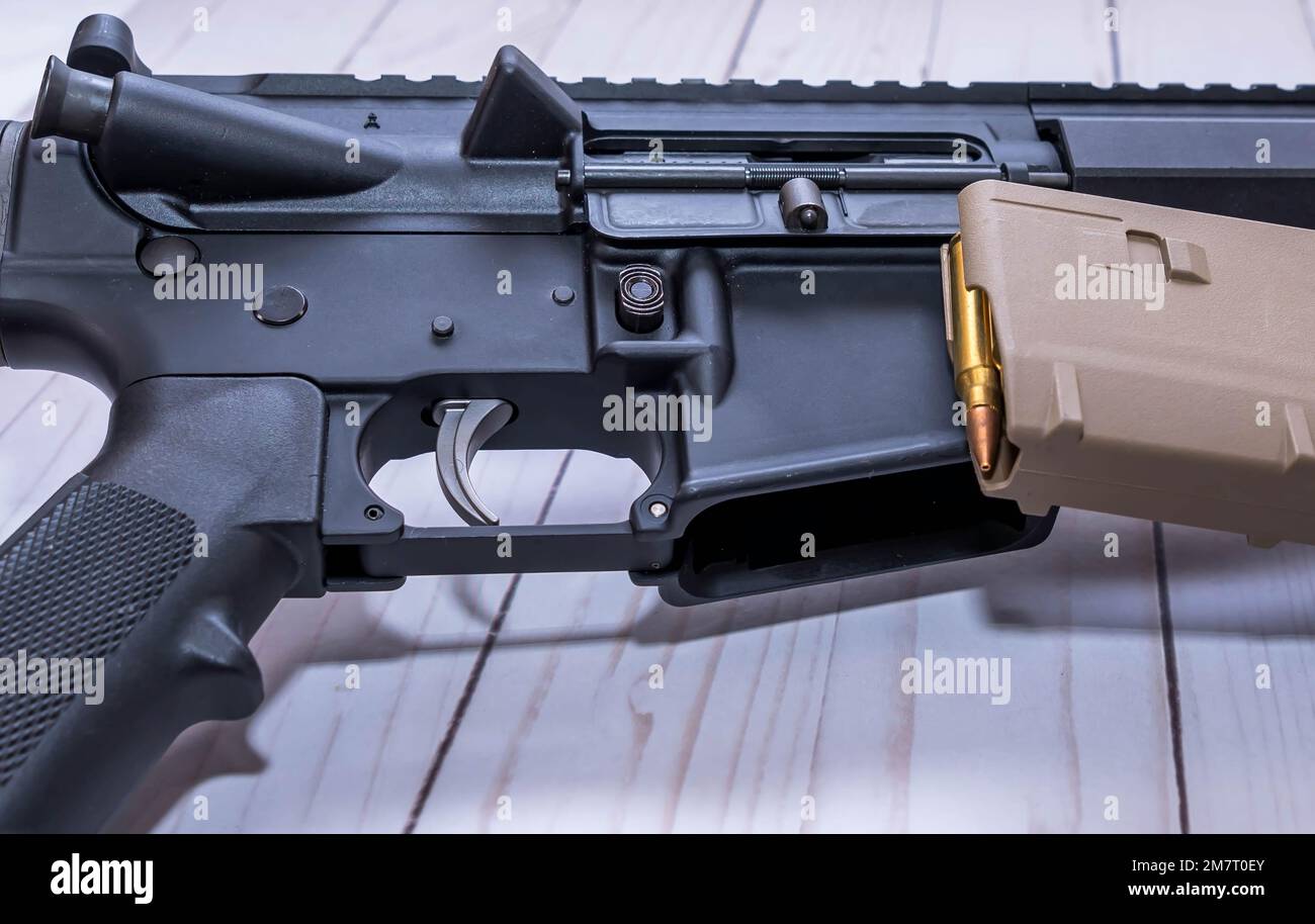 Un fucile AR15 smussato nel calibro 223 con accanto un caricatore caricato su fondo di legno bianco Foto Stock