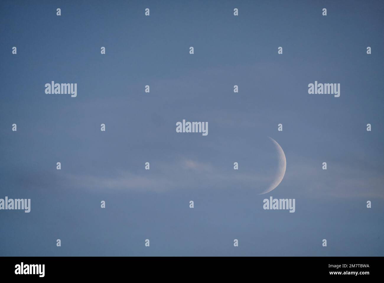 Una luna crescente è vista in basso a destra con nuvole bianche sussurre sulla luna, e un cielo blu profondo sera dietro di essa. Foto Stock