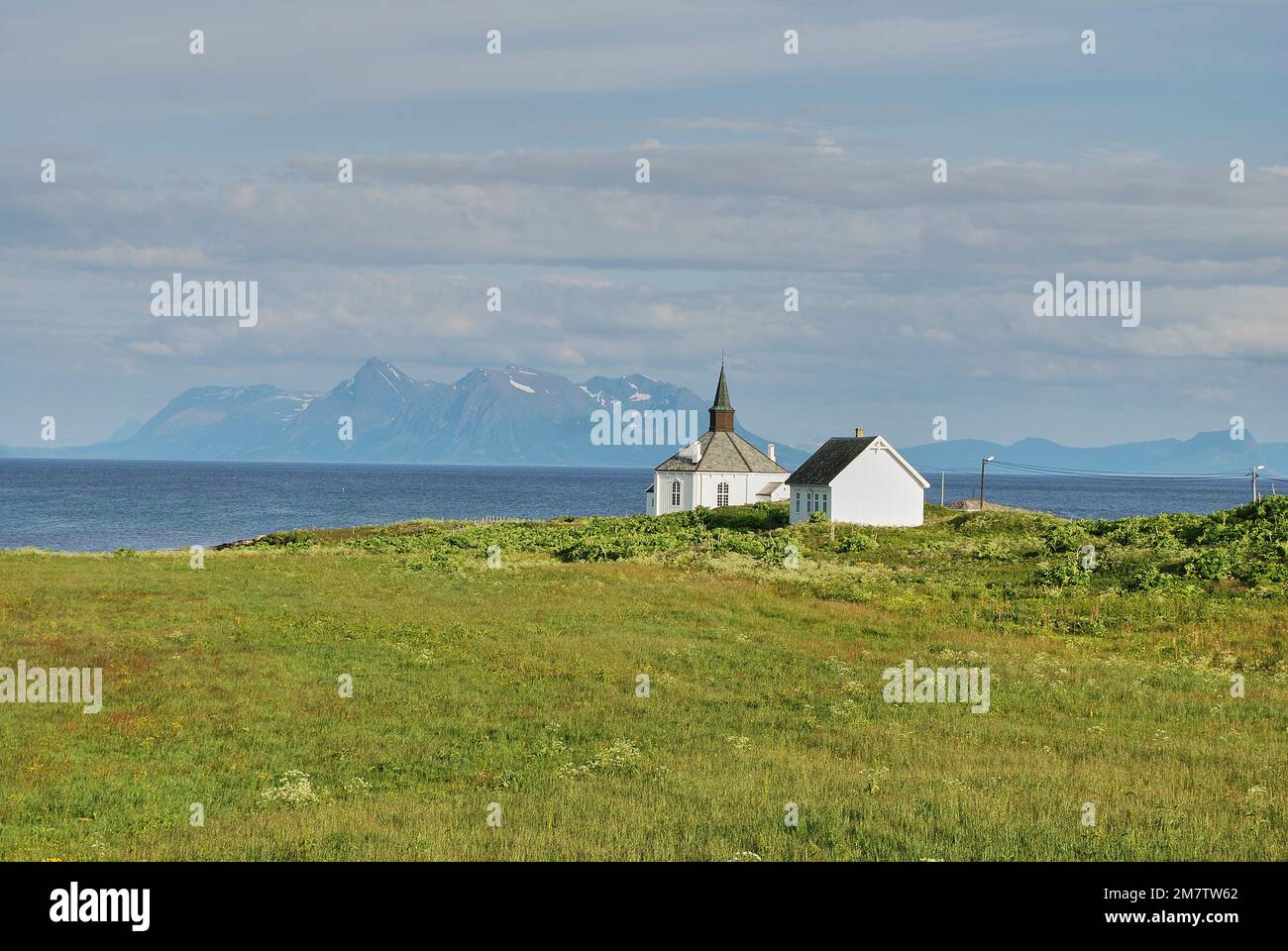 tipica piccola chiesa scandinava di legno bianco su un lussureggiante prato verde con l'oceano atlantico blu profondo e le montagne sullo sfondo in nort artico Foto Stock