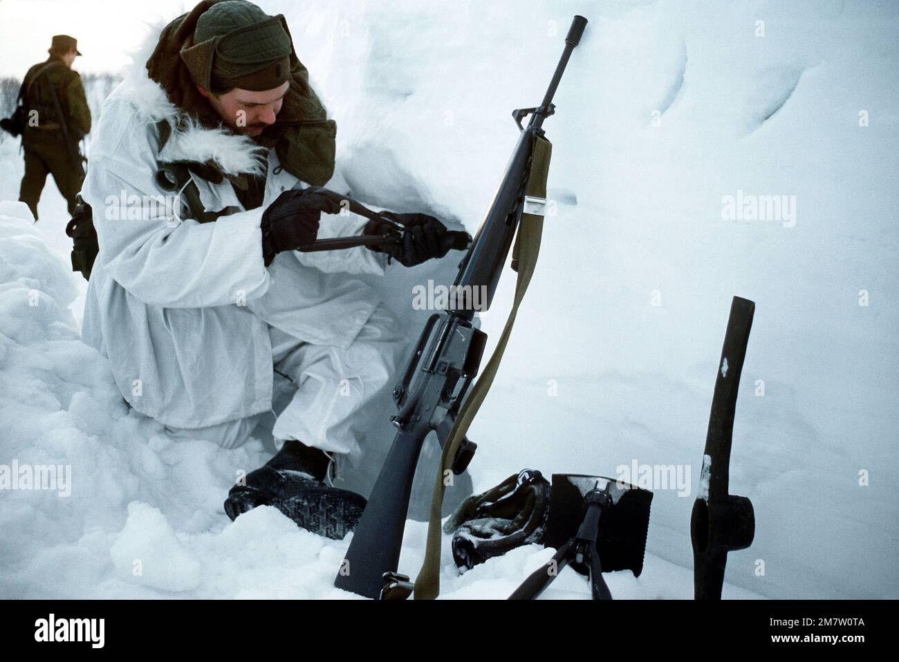 NEGLI STATI UNITI Air Force 1st LT. David L. Peters, un leader plotone con lo Squadrone 331st, utilizza uno strumento di radicamento per allargare l'ingresso alla sua grotta di neve (dormitori). Appoggiato alla grotta di neve è il suo fucile M-16A1. Base: Route e-6 Paese: Norvegia (NOR) Foto Stock