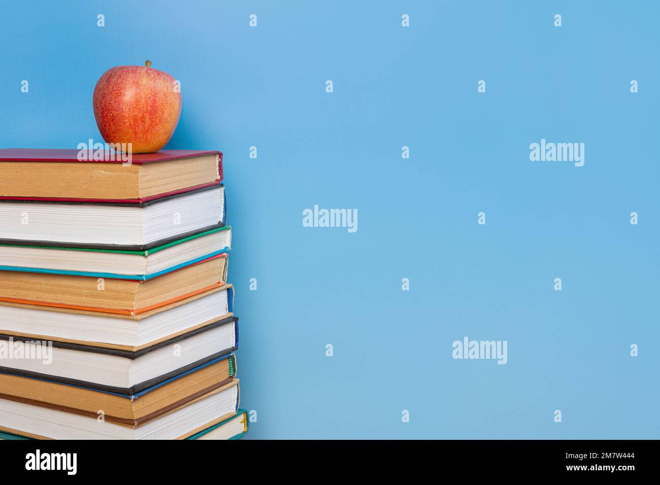 Pila di libri nella copertina colorata giaceva e libro con vecchie pagine e mela rossa su sfondo blu. Concetto di apprendimento per l'istruzione Foto Stock