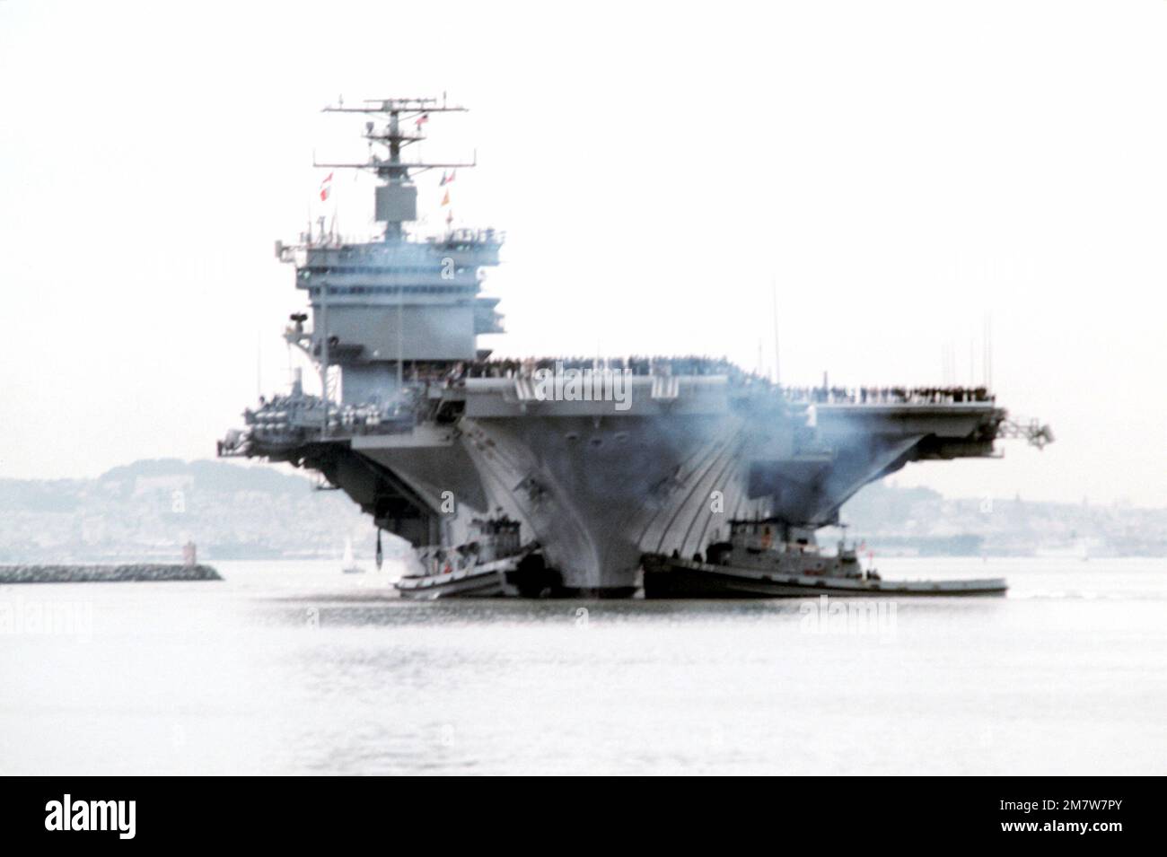 Prua in vista della portaerei nucleare USS ENTERPRISE (CVN-65) assistita in posizione di attracco da due grandi rimorchiatori portuali. Gli equipenti sono presiunti alla ferrovia mentre L'IMPRESA completa una breve crociera a seguito di recenti lavori di ristrutturazione che hanno incluso la ricostruzione della sovrastruttura. Base: Naval Air Station, Alameda Stato: California (CA) Paese: Stati Uniti d'America (USA) Foto Stock