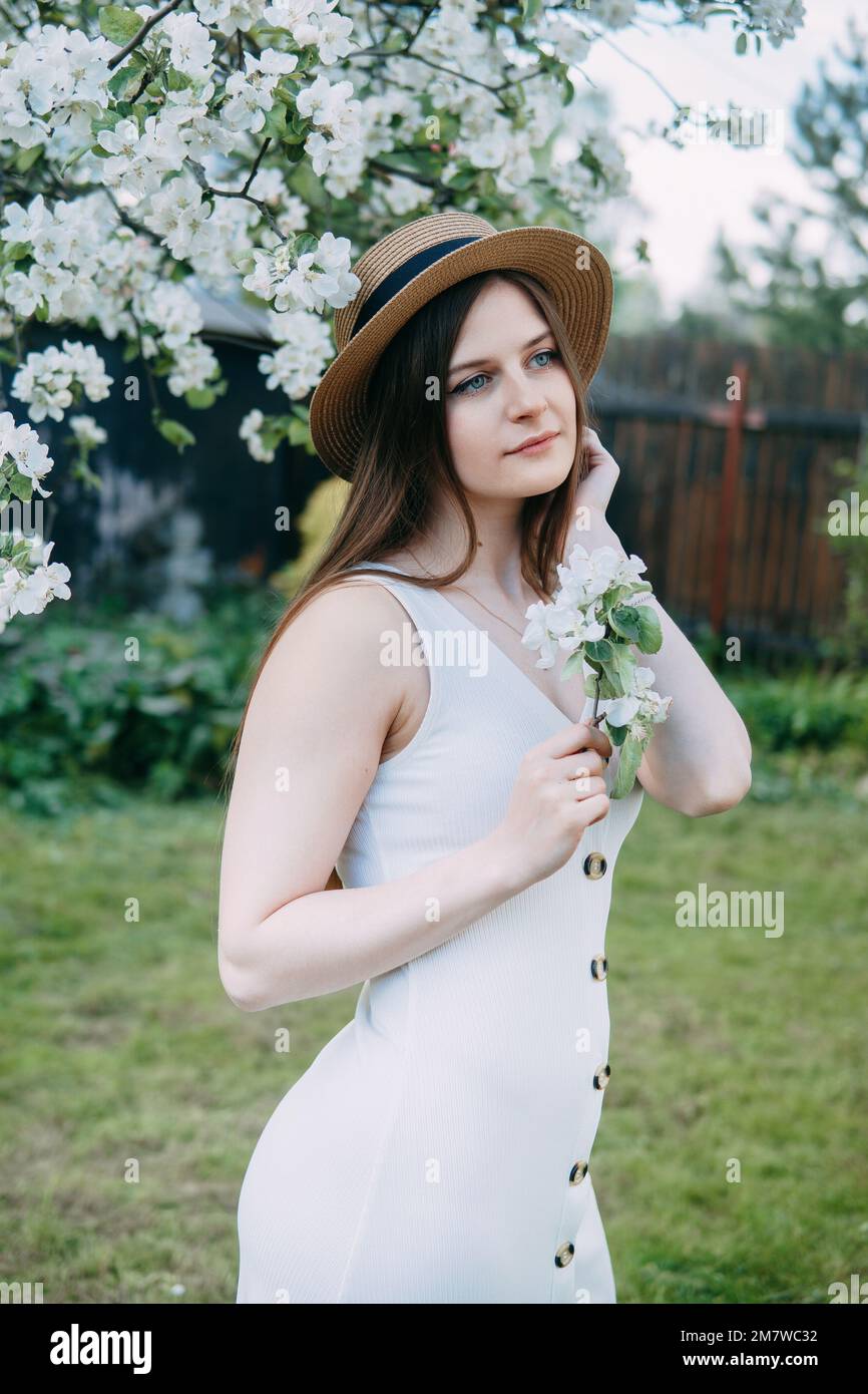 Bella giovane ragazza in vestito bianco e cappello in fiore Apple frutteto.  Alberi di mela fiorenti con fiori bianchi Foto stock - Alamy