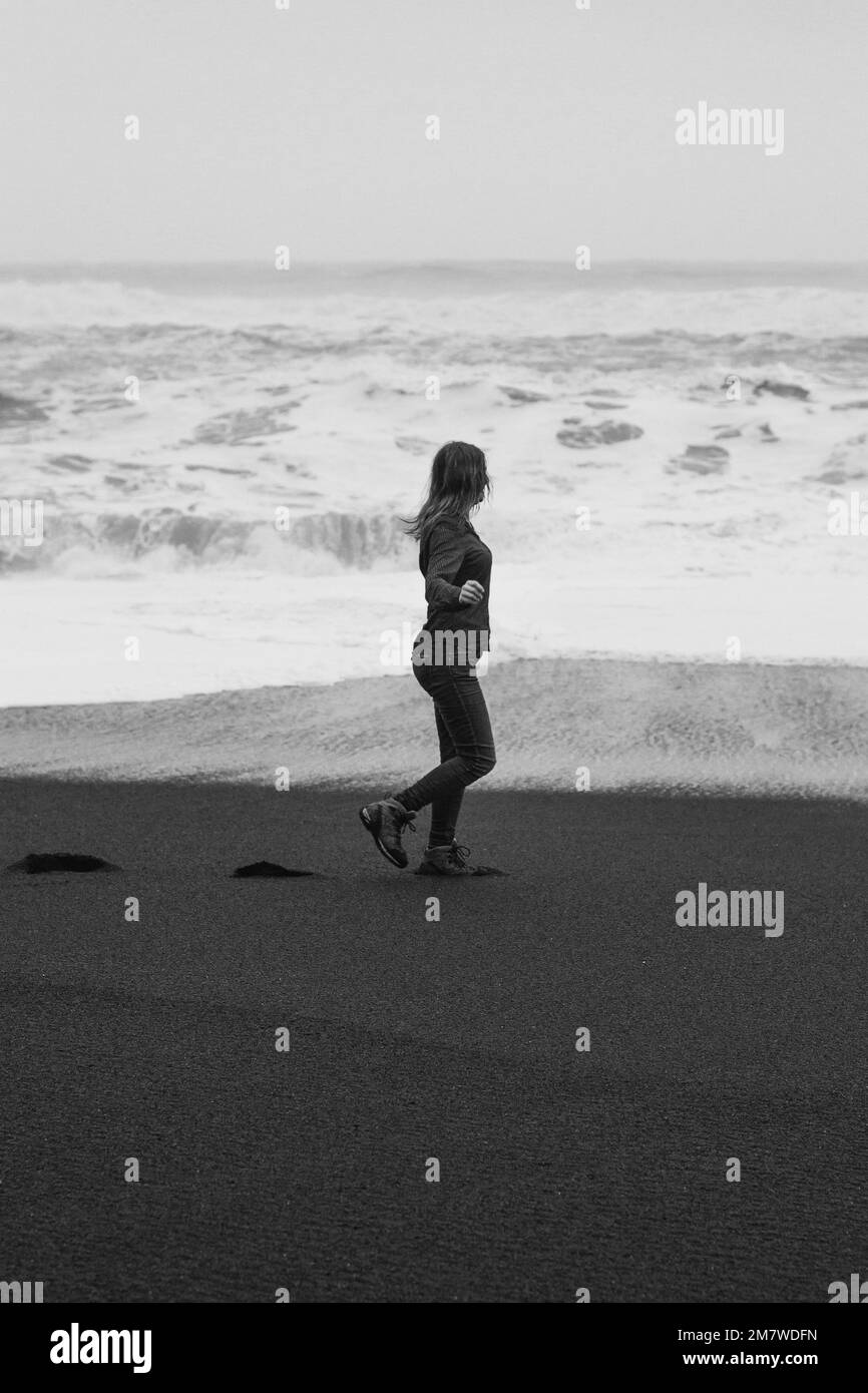 Donna attraente sulla spiaggia vuota Reynisfjara fotografia panoramica monocromatica Foto Stock