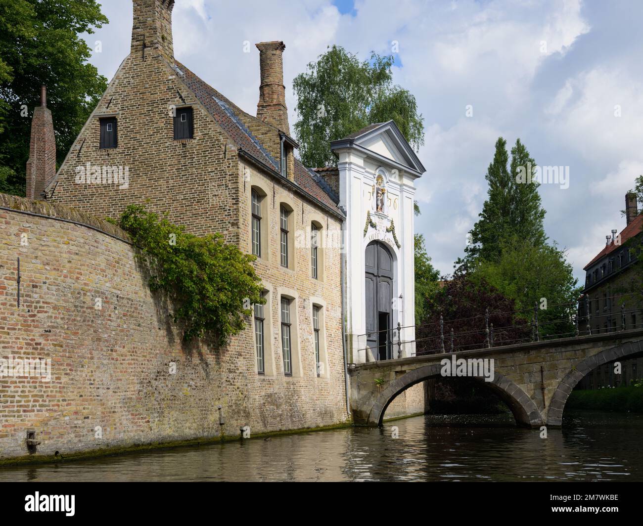 Bruges, Belgio-4 luglio 2022: Una vecchia casa su un canale con un ponte, luce del giorno, alberi Foto Stock