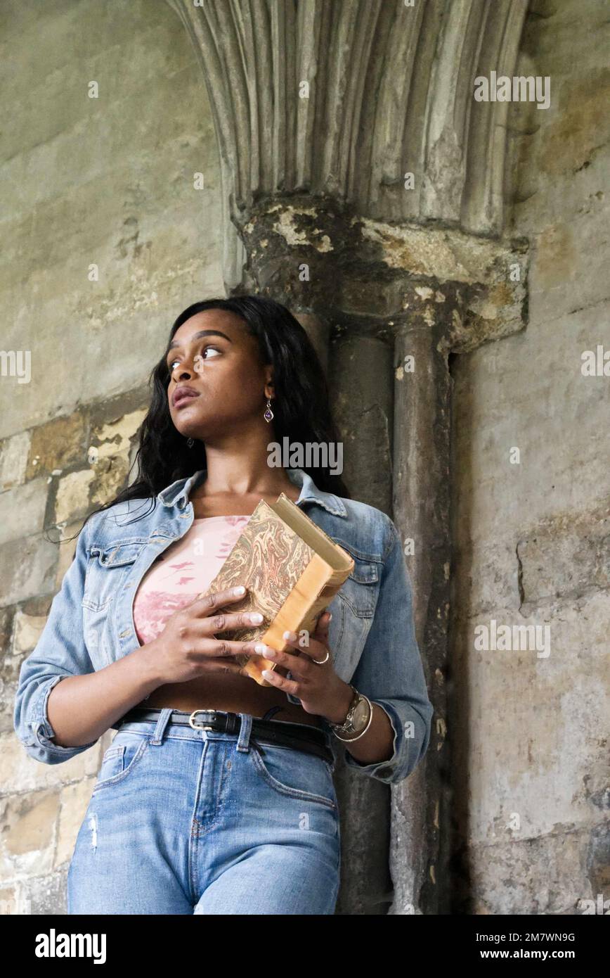 Una giovane donna con un libro in piedi accanto a una colonna medievale nel chiostro della cattedrale. Foto Stock