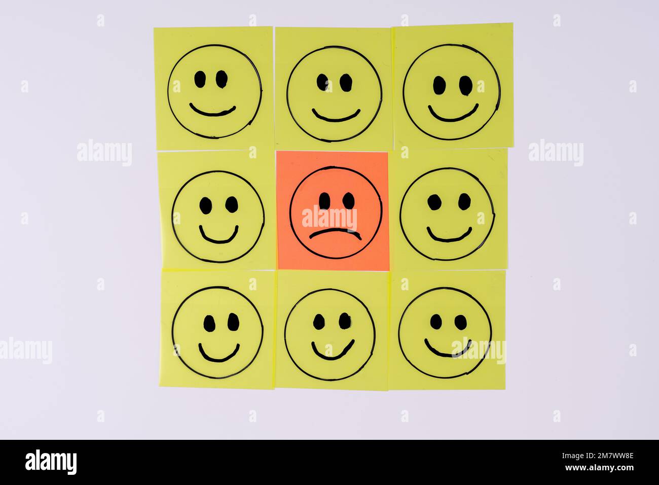 triste faccia di colore arancione surrouonded da felice gente smiley gialla disegnata come grafica su note appiccicose tramsparent isolate su uno sfondo bianco Foto Stock