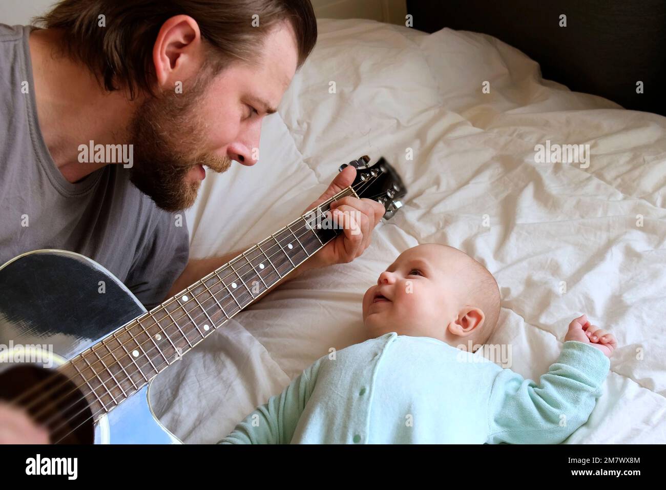 Padre bearded che gioca chitarra al suo bambino piccolo. Bambino che lo  guarda, ascoltando e sorridendo. Ritratto di Famiglia felice a casa.  Divertimento gioioso. Mani Foto stock - Alamy