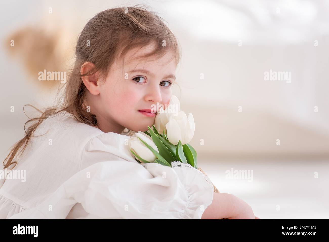 Primo piano ritratto di una bambina in abito bianco, abito da notte. Il bambino abbraccia un bouquet di tulipani bianchi freschi e delicati. Regalo per le vacanze, il Foto Stock