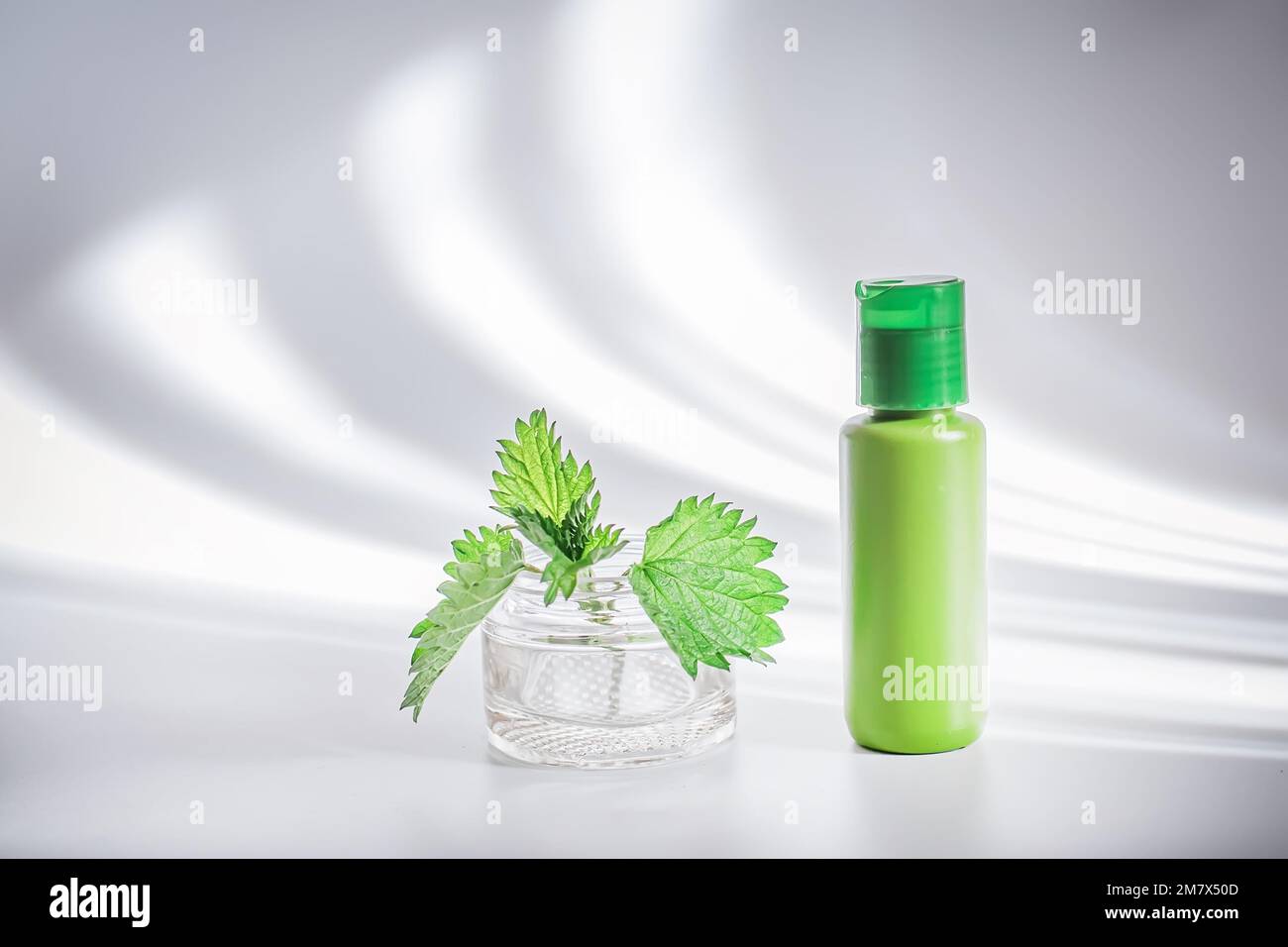 Crema corpo, o lozione con foglie di ortica in un contenitore di plastica su uno sfondo bianco con ombre alla moda. Foto Stock