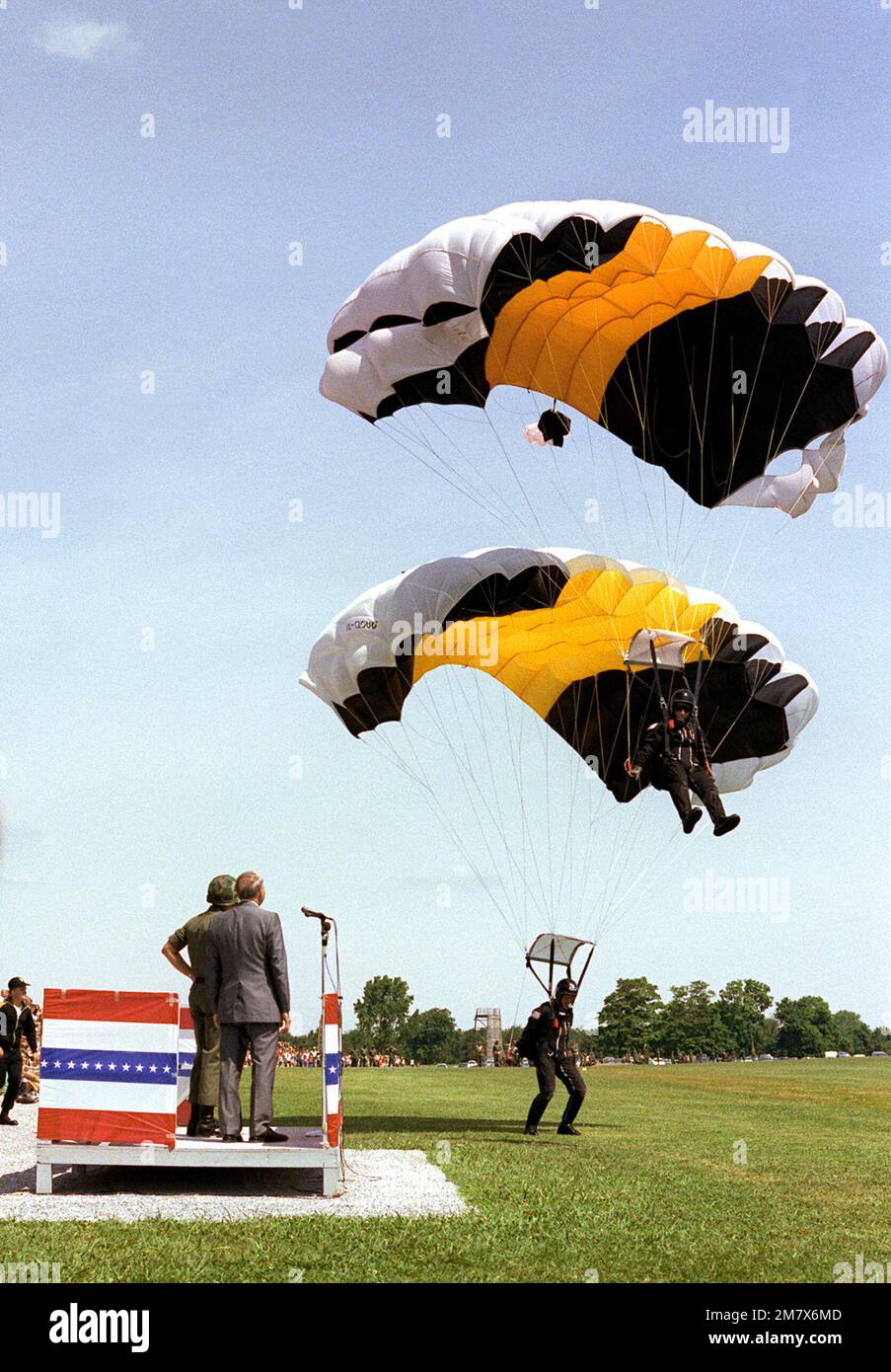 Il Segretario dell'Esercito John O. Marsh guarda come due membri di una squadra di quattro uomini terra durante una performance del Screaming Eagles Sports Parachute Club alla Division Review. Base: Fort Campbell Stato: Kentucky (Kentucky) Nazione: Stati Uniti d'America (USA) Foto Stock