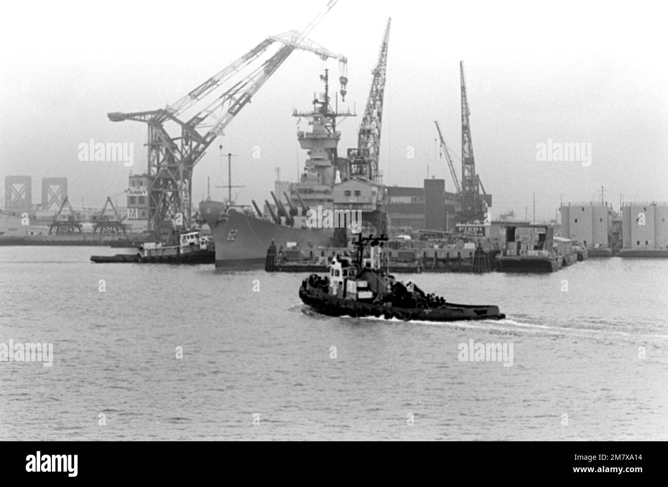 Una vista di prua del porto del NEW JERSEY (BB-62), mentre i rimorchiatori lungo il lato a dritta si preparano a trainare la corazzata lontano dal suo ormeggio prima delle prove in mare. Il New Jersey sarà rimesso in funzione nel gennaio 1983. Base: Long Beach Naval Shipyard Stato: California (CA) Paese: Stati Uniti d'America (USA) Foto Stock