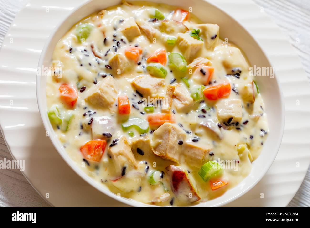 Zuppa cremosa di riso selvatico tacchino con patate rosse. carota, sedano, spezie ed erbe aromatiche in ciotola bianca su tavola di legno Foto Stock