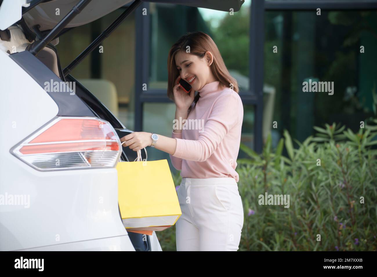 La giovane donna mette le borse della spesa in auto e parla al telefono. Foto Stock