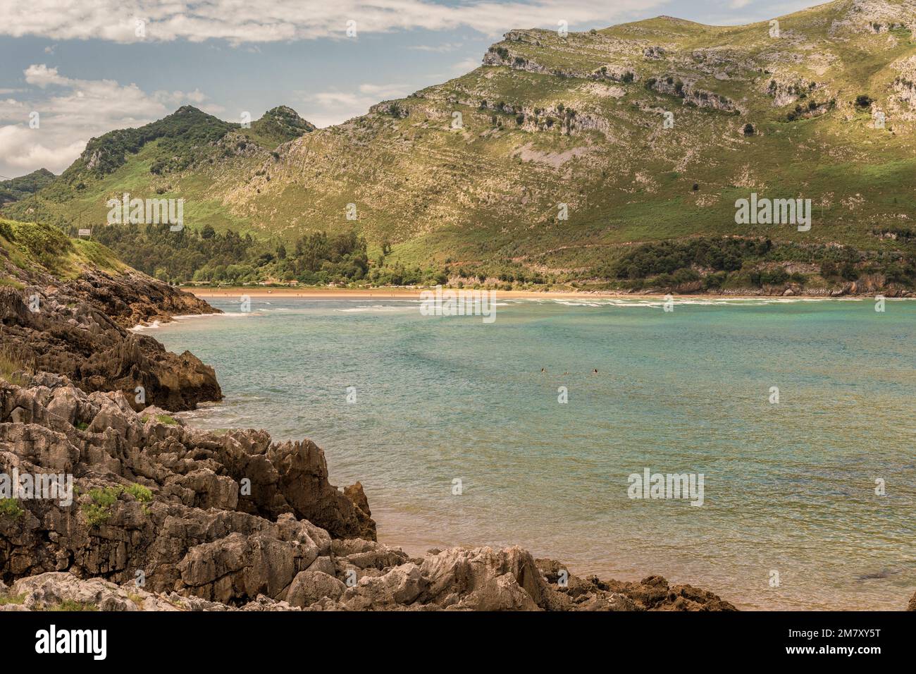 Tre donne che fanno il bagno sulla spiaggia di Oriñon con le rocce e la montagna verde sullo sfondo in Cantabria, Spagna Foto Stock