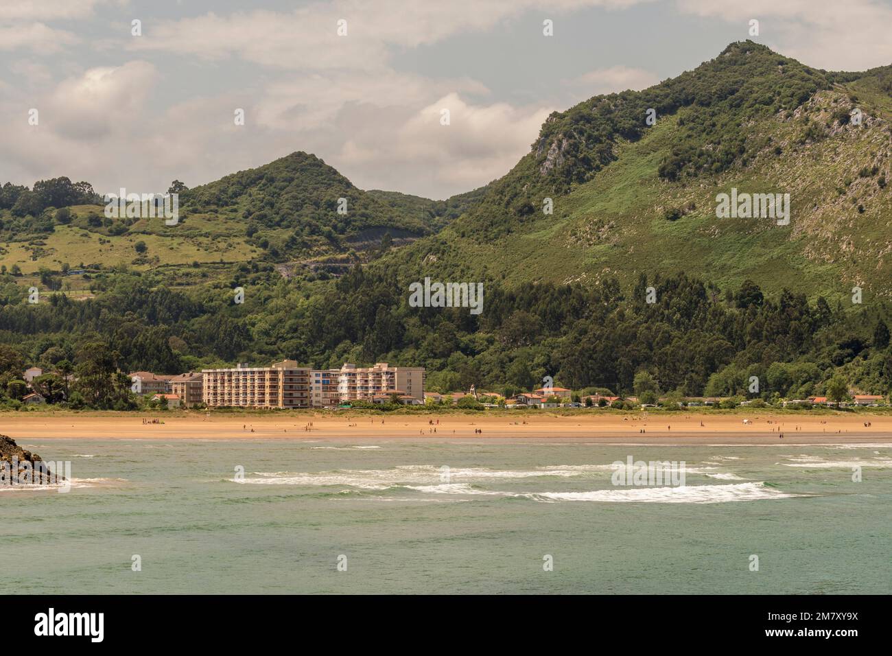 Vista di edifici di appartamenti, case e persone che prendono il sole sulla sabbia della spiaggia di Oriñon dalla città di Islares in Cantabria, Spagna Foto Stock