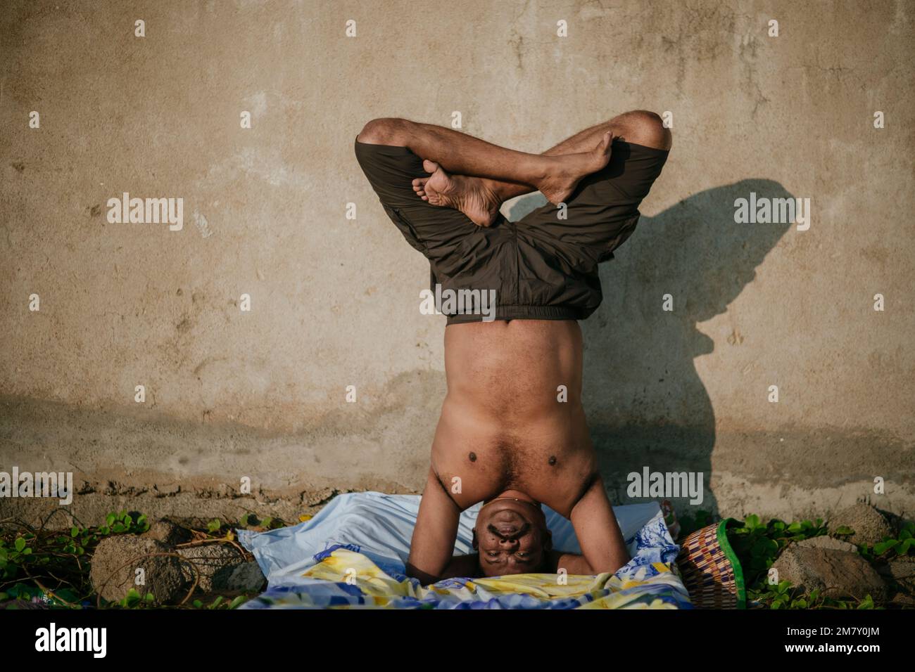 Modello maschile indiano che esegue la postura di Yoga del supporto per la testa Foto Stock