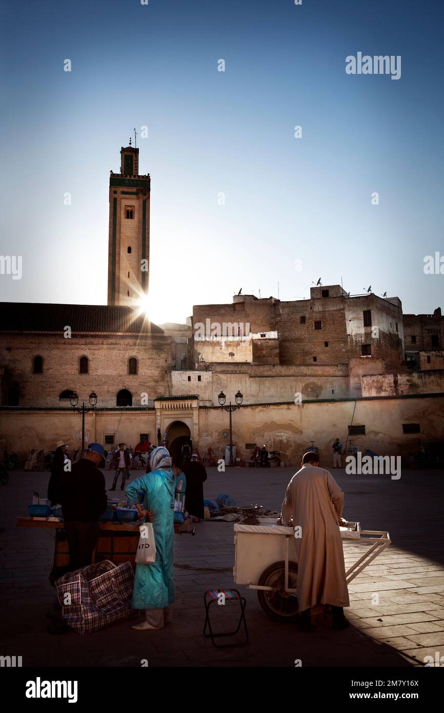 Fez, Marocco-25 aprile 2014: Tramonto in una piazza dove marocchini vendere cibo e vestiti sul mercato piccolo, molte persone a guardare e acquistare, altri res Foto Stock