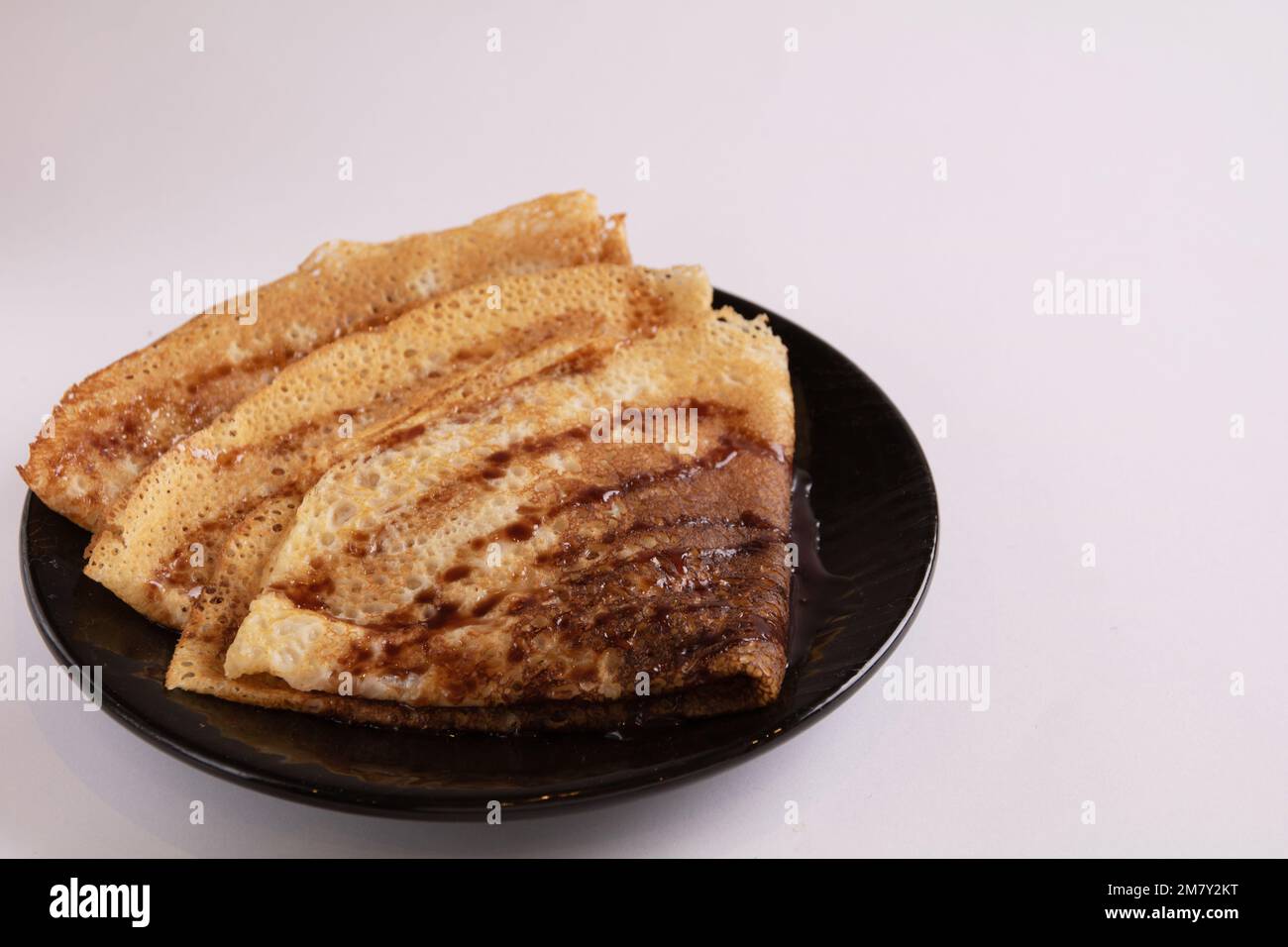 foto frittelle sottili sgocciolate con sciroppo di cioccolato su un piatto rotondo nero Foto Stock