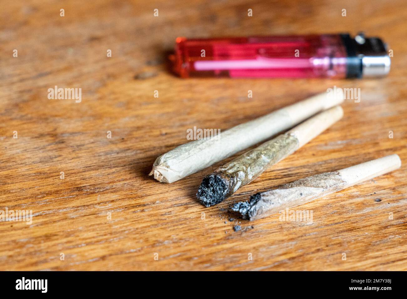 Sigaretta di cannabis con accendino su tavolo di legno Foto Stock