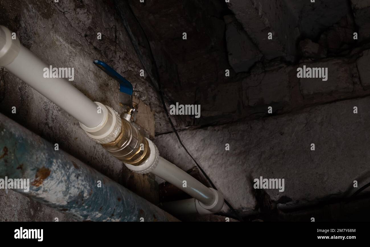 Rubinetto di acqua tubo di plastica in posizione aperta su sfondo sfocato della parete del seminterrato della casa con illuminazione locale Foto Stock