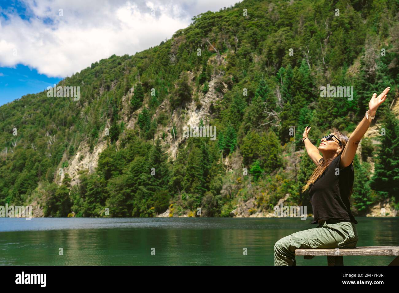Donna seduta sul molo sulla riva di un grande lago immerso in un'oasi di natura. Foto Stock